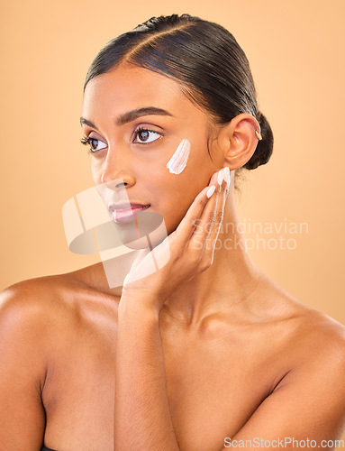 Image of Face, beauty skincare and woman with cream in studio isolated on a brown background. Dermatology, cosmetics idea and thinking Indian female model with lotion, creme or moisturizer for skin health.