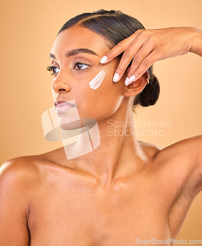 Image of Face, skincare idea and woman with cream in studio isolated on a brown background. Dermatology, cosmetics and thinking Indian female model with lotion, beauty creme or moisturizer for skin health.