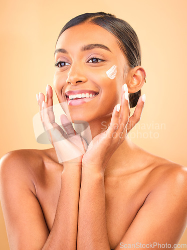 Image of Face, skincare smile and woman with cream in studio isolated on a brown background. Dermatology cosmetics, thinking and happy Indian female model apply lotion, creme and moisturizer for healthy skin.