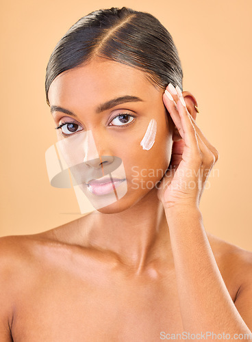 Image of Face portrait, skincare and woman with cream in studio isolated on brown background. Dermatology, serious cosmetics and confident Indian female model with lotion, creme or moisturizer for skin health