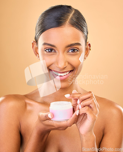 Image of Face, skincare and woman with cream jar in studio isolated on a brown background. Dermatology cosmetics, portrait and happy Indian female apply lotion, creme and moisturizer product for healthy skin.