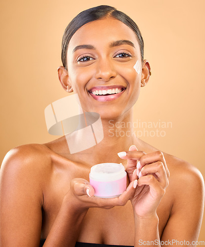 Image of Face, skincare and woman with cream jar in studio isolated on a brown background. Dermatology cosmetics, portrait and happy Indian female apply lotion, creme and moisturizer product for healthy skin.