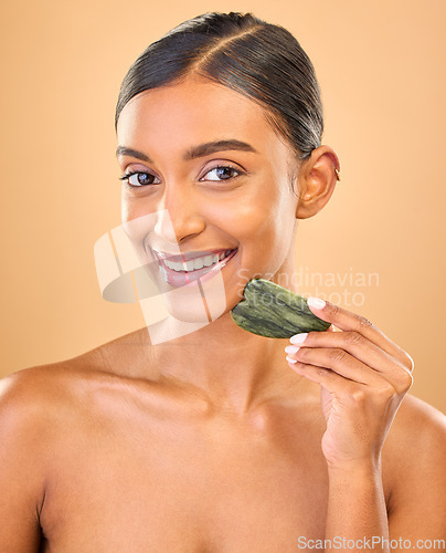 Image of Face smile, skincare and woman with gua sha in studio isolated on a brown background. Dermatology portrait, massage and happy Indian female model with jade crystal or stone for healthy skin treatment