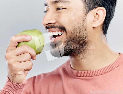 Image of Enjoying, happy and an Asian man eating an apple isolated on a white background in a studio. Smile, food and a Chinese guy taking a bite from a fruit for nutrition, diet or hungry on a backdrop