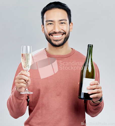 Image of Portrait, champagne and cheers with a man in studio on a gray background holding a bottle for celebration. Glass, alcohol and toast with a handsome young man celebrating the new year tradition