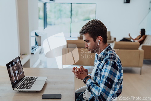 Image of The man sitting at a table in a modern living room, with headphones using a laptop for business video chat, conversation with friends and entertainment