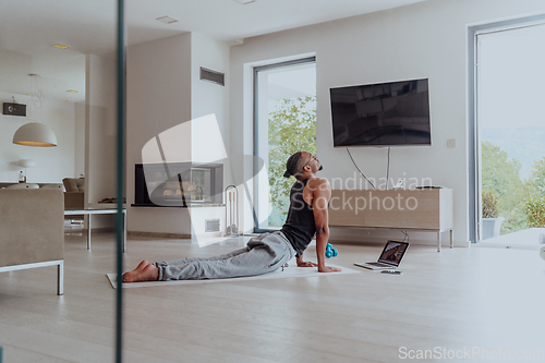 Image of Training At Home. Sporty man doing training while watching online tutorial on laptop, exercising in living room, free space