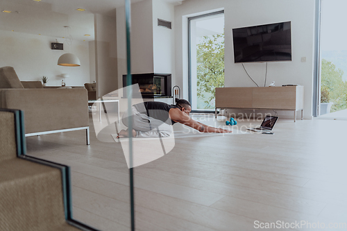 Image of Training At Home. Sporty man doing training while watching online tutorial on laptop, exercising in living room, free space