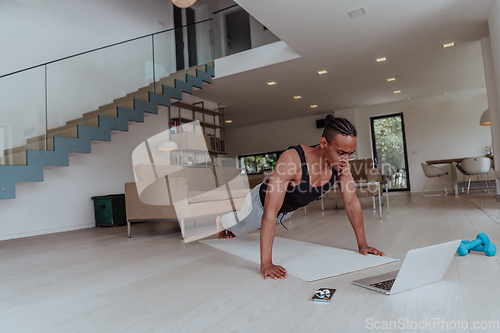 Image of Training At Home. Sporty man doing training while watching online tutorial on laptop, exercising in living room, free space