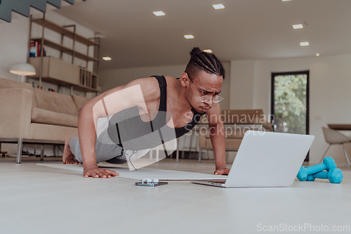 Image of Training At Home. Sporty man doing training while watching online tutorial on laptop, exercising in living room, free space