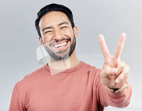 Image of Portrait, peace sign and laughing Asian man in studio isolated on a gray background. Face, v emoji and happy, smiling or funny, young and confident male model with hand gesture or peaceful symbol.