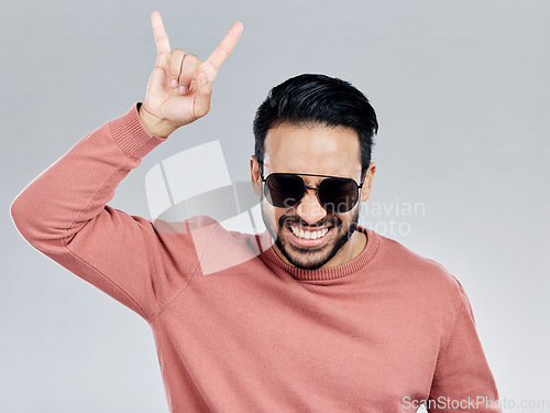 Image of Portrait, rock on and hand gesture with a man in studio on a gray background feeling crazy or energetic. Face, rocker or hardcore and a male posing with a devil horns sign or symbol at a concert