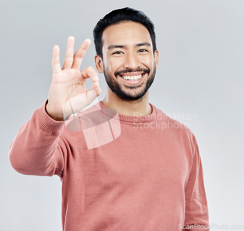 Image of Hand, portrait and okay sign by man in studio with yes, vote or approval gesture against grey background. Finger, emoji and perfect symbol by asian male happy with decision, thank you or satisfied