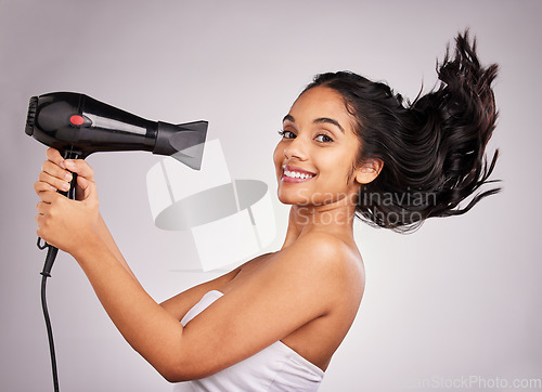 Image of Portrait, blow dry and hair with a woman in studio on a gray background holding a beauty appliance. Salon, smile and hairdryer with an attractive young female model drying her hairstyle with wind