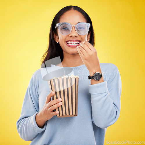 Image of Woman is eating popcorn, watching tv and happy in portrait with snack for movie on yellow studio background. Streaming service, cinema and food with corn treat, female smile with funky sunglasses