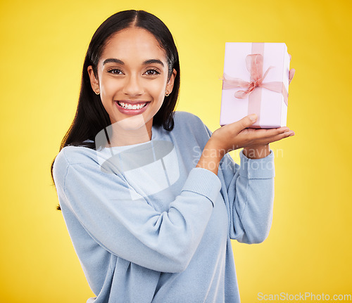 Image of Woman smile, portrait and gift box in a studio happy from surprise present for birthday. Giveaway prize, isolated and yellow background of a young female student feeling positive and cheerful