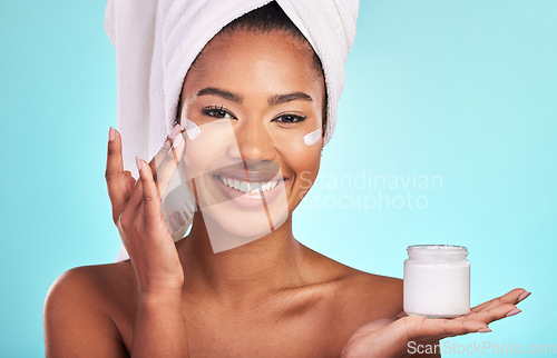 Image of Skincare, beauty and portrait of black woman with cream, towel and smile in bathroom routine or skin glow on blue background. Cosmetics, facial and African model with lotion product in hand in studio