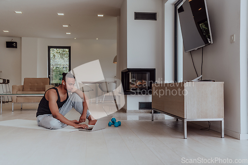 Image of Training At Home. Sporty man doing training while watching online tutorial on laptop, exercising in living room, free space