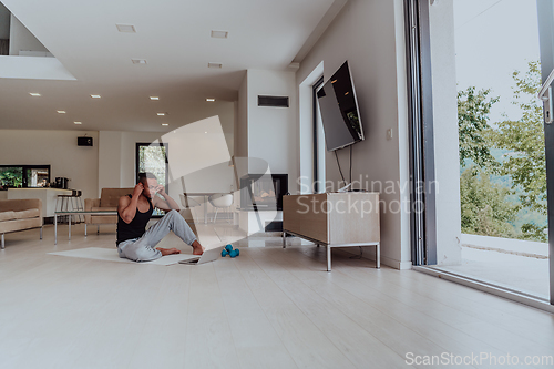 Image of Training At Home. Sporty man doing training while watching online tutorial on laptop, exercising in living room, free space