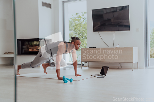 Image of Training At Home. Sporty man doing training while watching online tutorial on laptop, exercising in living room, free space