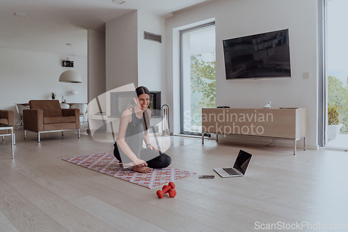 Image of Young Beautiful Female Exercising, Stretching and Practising Yoga with Trainer via Video Call Conference in Bright Sunny Loft Apartment. Healthy Lifestyle, Wellbeing and Mindfulness Concept.