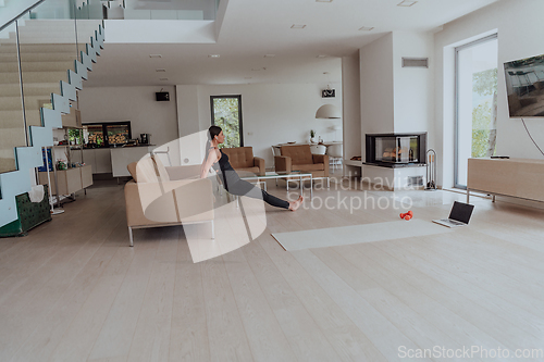 Image of Young Beautiful Female Exercising, Stretching and Practising Yoga with Trainer via Video Call Conference in Bright Sunny Loft Apartment. Healthy Lifestyle, Wellbeing and Mindfulness Concept.