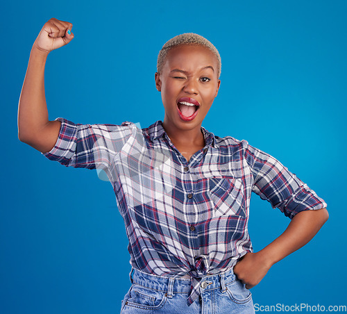 Image of Wink, arm flex and portrait of black woman in studio for empowerment, confident and success. Achievement, hard work and pride with female isolated on blue background for power, strong or motivation