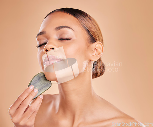 Image of Beauty, facial and massage with gua sha by woman in studio for skincare, cosmetic or facelift on brown background. Calm, face and anti aging tool for girl model relax with luxury dermatology wellness