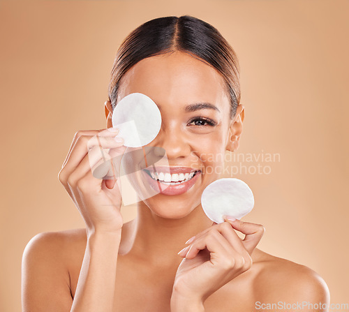 Image of Face, cotton pad and woman with makeup, dermatology and happiness against a brown studio background. Portrait, female or lady with smile, cosmetics and organic facial with foundation remover and joy