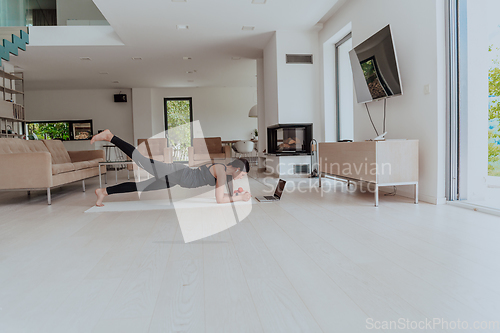 Image of Young Beautiful Female Exercising, Stretching and Practising Yoga with Trainer via Video Call Conference in Bright Sunny House. Healthy Lifestyle, Wellbeing and Mindfulness Concept.