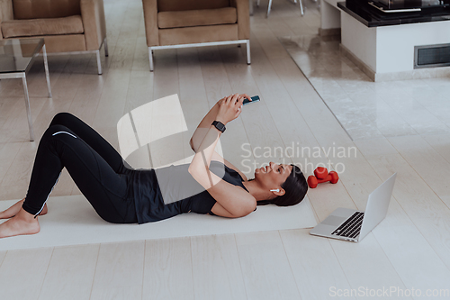 Image of Sportswoman using a smartphone while resting and lying on floor of modern house