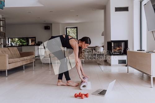 Image of A young woman in sports clothes preparing sports equipment for online training in her living room