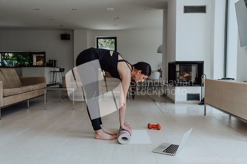 Image of A young woman in sports clothes preparing sports equipment for online training in her living room