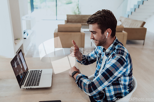 Image of The man sitting at a table in a modern living room, with headphones using a laptop for business video chat, conversation with friends and entertainment