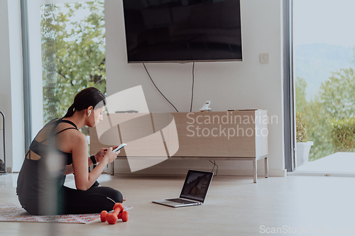 Image of Young woman in sportswear using laptop and smartphone for online training in living room at home during corona virus and social distancing