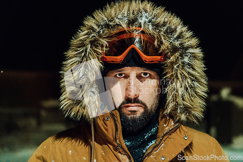 Image of Head shot of a man in a cold snowy area wearing a thick brown winter jacket, snow goggles and gloves on a cold Scandinavian night. Life in the cold regions of the country.