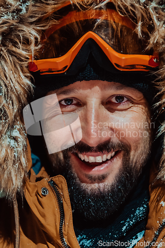 Image of Head shot of a man in a cold snowy area wearing a thick brown winter jacket, snow goggles and gloves on a cold Scandinavian night. Life in the cold regions of the country.