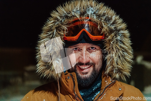 Image of Head shot of a man in a cold snowy area wearing a thick brown winter jacket, snow goggles and gloves on a cold Scandinavian night. Life in the cold regions of the country.