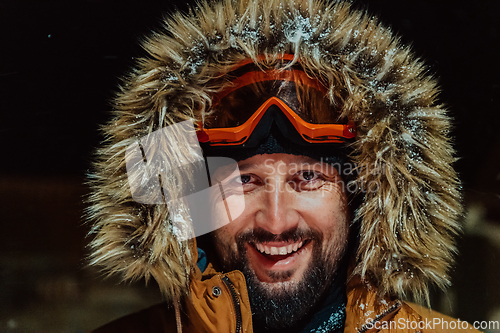 Image of Head shot of a man in a cold snowy area wearing a thick brown winter jacket, snow goggles and gloves on a cold Scandinavian night. Life in the cold regions of the country.