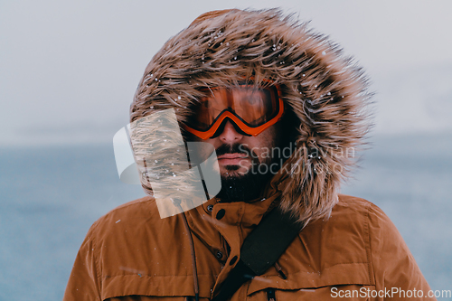 Image of Headshot photo of a man in a cold snowy area wearing a thick brown winter jacket, snow goggles and gloves. Life in cold regions of the country.