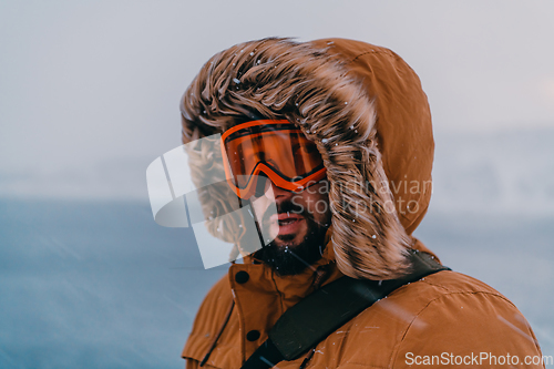 Image of Headshot photo of a man in a cold snowy area wearing a thick brown winter jacket, snow goggles and gloves. Life in cold regions of the country.