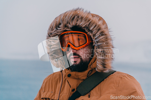 Image of Headshot photo of a man in a cold snowy area wearing a thick brown winter jacket, snow goggles and gloves. Life in cold regions of the country.