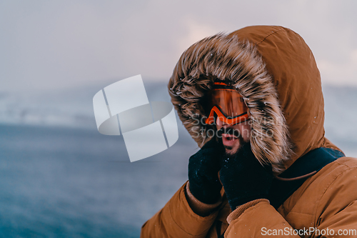 Image of Headshot photo of a man in a cold snowy area wearing a thick brown winter jacket, snow goggles and gloves. Life in cold regions of the country.