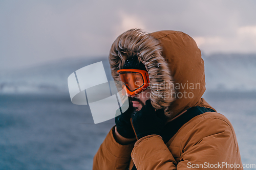 Image of Headshot photo of a man in a cold snowy area wearing a thick brown winter jacket, snow goggles and gloves. Life in cold regions of the country.