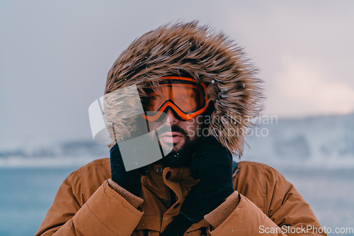 Image of Headshot photo of a man in a cold snowy area wearing a thick brown winter jacket, snow goggles and gloves. Life in cold regions of the country.