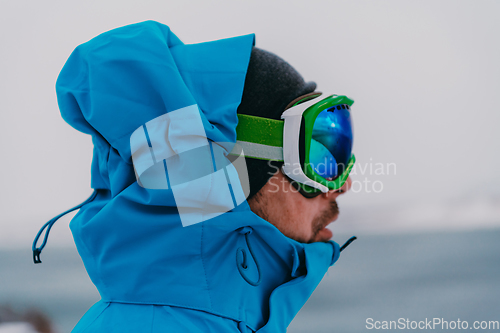 Image of Headshot photo of a man in a cold snowy area wearing a thick blue winter jacket, snow goggles and gloves. Life in cold regions of the country.