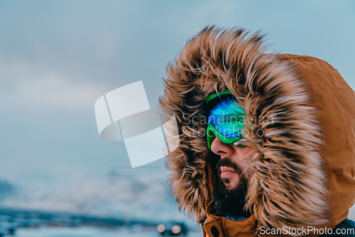 Image of Headshot photo of a man in a cold snowy area wearing a thick brown winter jacket, snow goggles and gloves. Life in cold regions of the country.