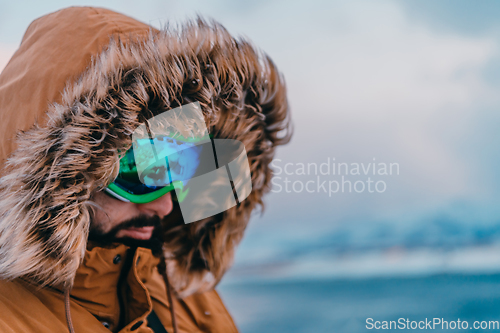 Image of Headshot photo of a man in a cold snowy area wearing a thick brown winter jacket, snow goggles and gloves. Life in cold regions of the country.