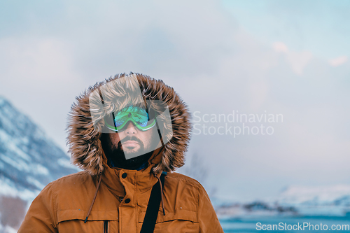 Image of Headshot photo of a man in a cold snowy area wearing a thick brown winter jacket, snow goggles and gloves. Life in cold regions of the country.