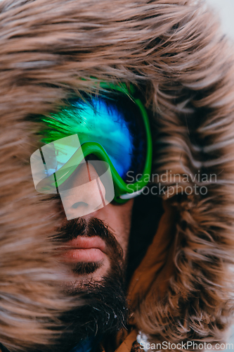 Image of Headshot photo of a man in a cold snowy area wearing a thick brown winter jacket, snow goggles and gloves. Life in cold regions of the country.